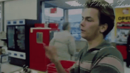 a man in a green and pink striped shirt is standing in front of a sign that says river phoenix fans