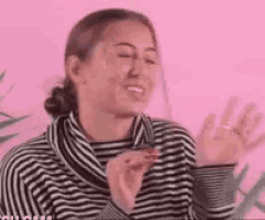 a woman in a striped shirt is smiling and waving her hands in front of a pink wall .