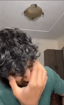 a man with curly hair is covering his face with his hand while a pot is hanging from the ceiling .