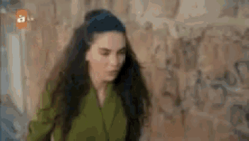 a woman in a green jacket is standing in front of a brick wall .