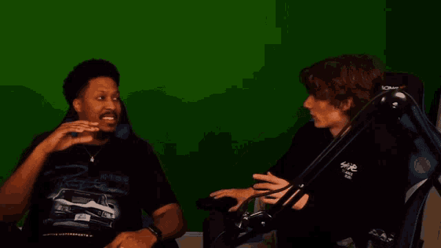two men are sitting in front of a green screen and one of them is wearing a shirt that says ' r ' on it