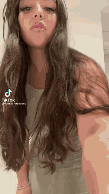 a woman with long hair is wearing a white tank top and a tik tok video