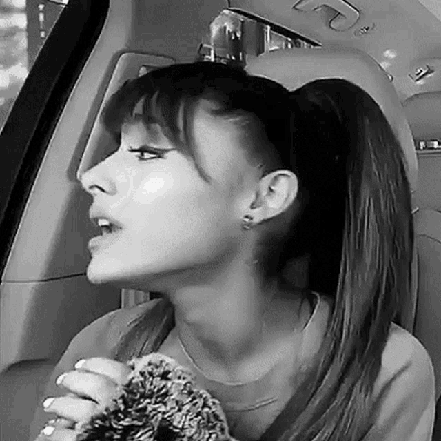 ariana grande is wearing a ponytail and holding a teddy bear in a car .