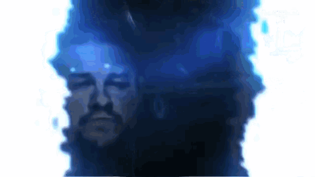 a close up of a man 's face in a dark room with a blue background .