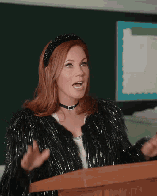 a woman in a black fur coat stands at a podium with her hands outstretched