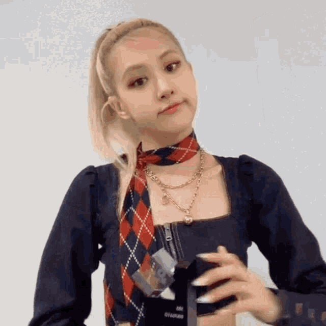 a woman wearing a plaid scarf around her neck and a necklace is standing in front of a white wall .