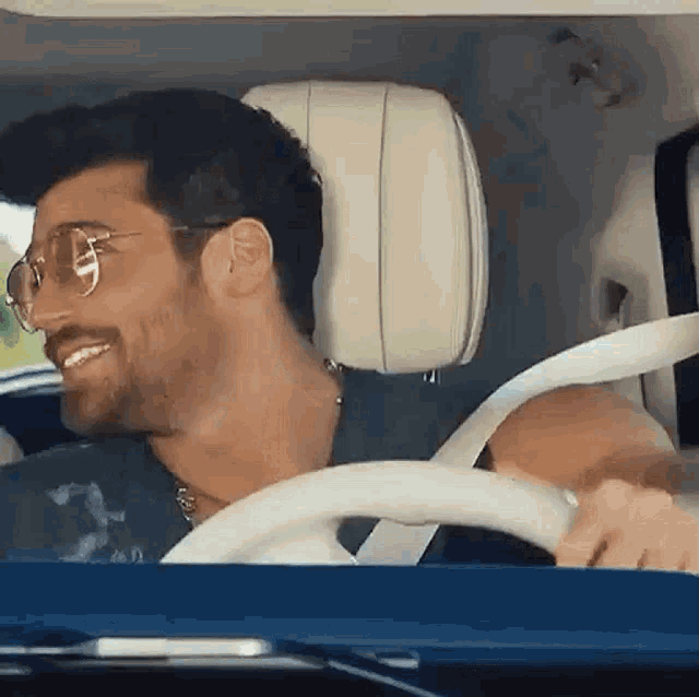 a man wearing glasses and a seat belt is driving a car .