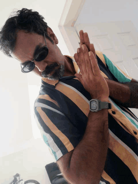 a man wearing sunglasses and a striped shirt has a watch on his wrist