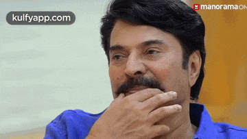 a man with a mustache is covering his mouth with his hand while wearing a blue shirt .
