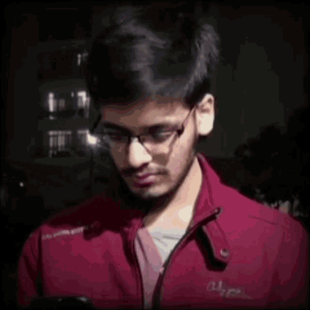 a young man wearing glasses and a red jacket with the word alpha on the front