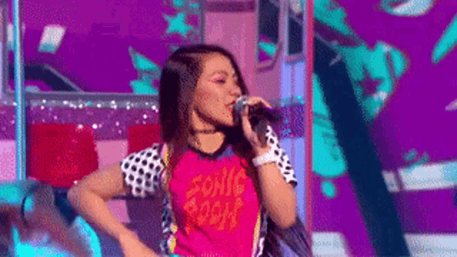 a woman is singing into a microphone while wearing a sonic the hedgehog shirt .