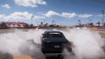a blue car is driving down a road with smoke coming out of its tires