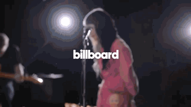 a woman singing into a microphone in front of the billboard logo