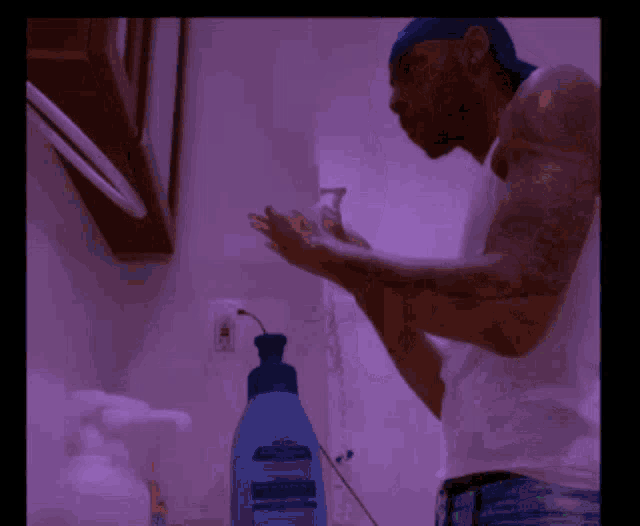a man in a white tank top is washing his hands in front of a bottle of dawn dish soap