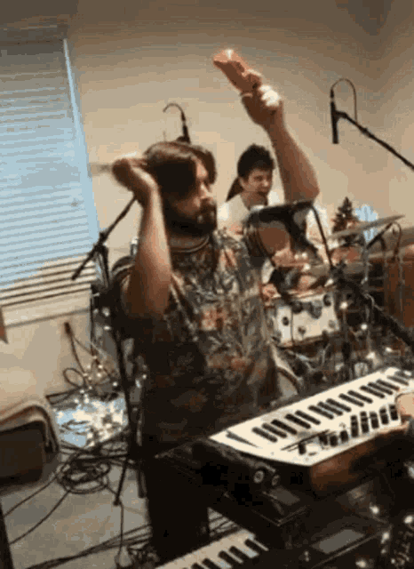 a man is playing a keyboard while another man plays drums in the background