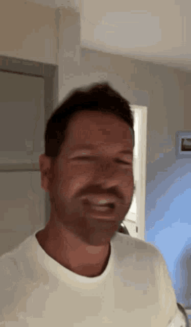 a man with a beard wearing a white t-shirt is smiling