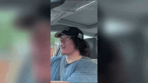 a man wearing a hat and a blue shirt is driving a car .