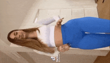 a woman in a white crop top and blue pants is standing in a room .