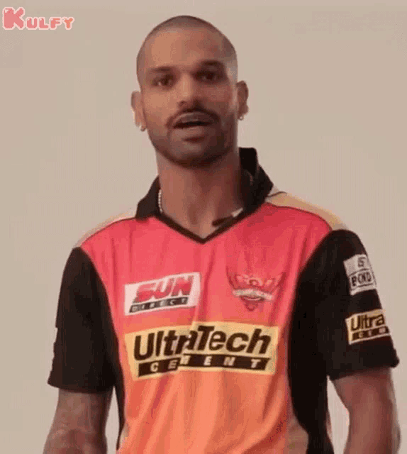 a man wearing a sun direct ultratech jersey is standing in front of a white wall .