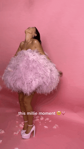 a woman in a pink feathered dress is standing on a pink background