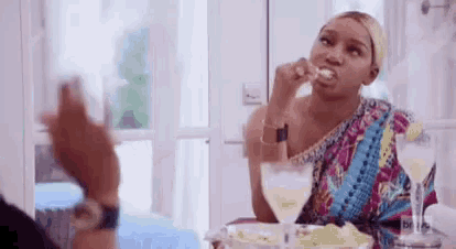 a woman is sitting at a table eating a piece of food and drinking a glass of wine .