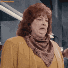 a woman wearing a scarf around her neck and a yellow jacket is making a funny face .