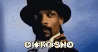 snoop dogg is wearing a top hat and talking on a cell phone while wearing a suit and tie .