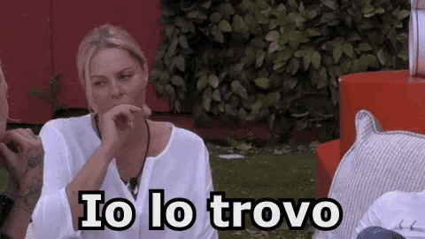 a woman in a white shirt is sitting in the grass with the words io lo trovo written on the bottom of her face .