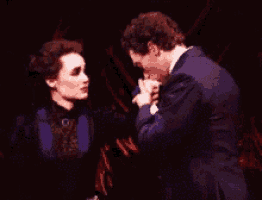 a man is kissing a woman 's hand on a stage in a dark room .