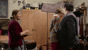a woman in a red sweater is talking to a man and woman in a room