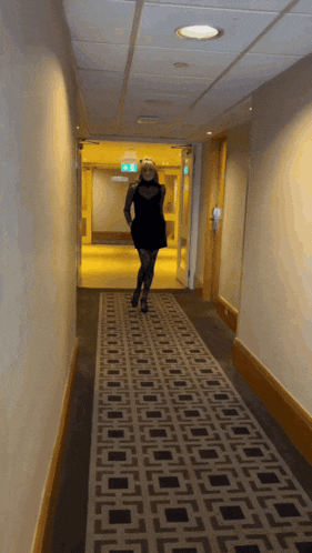 a woman in a black dress is walking down a hallway with a sign that says exit