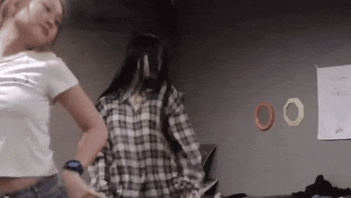 two women are dancing in front of a wall with the letters 00 on it