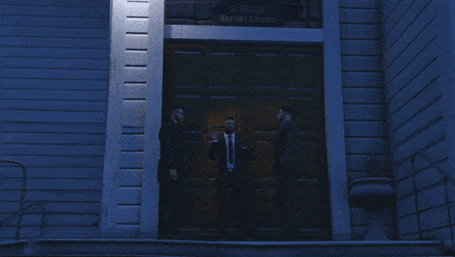three men in suits are standing in front of a large wooden door