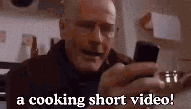 a bald man with glasses is holding a cell phone in his hand and says a cooking short video .