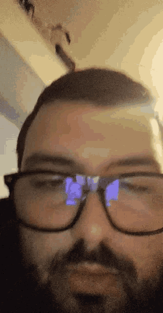 a man with glasses and a beard looks at the camera with his eyes closed