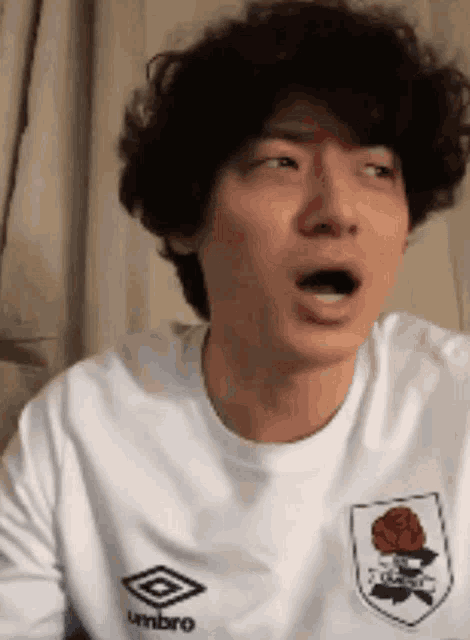 a man with curly hair is wearing a white t-shirt with umbro on it .