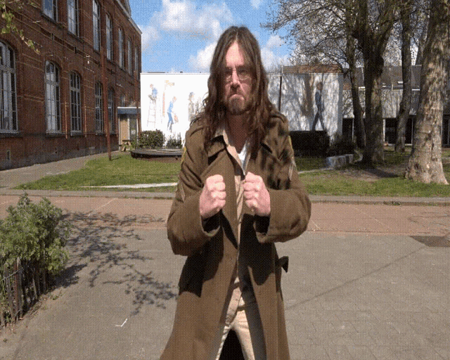 a man with long hair and a beard stands in front of a building with a sign that says ' a '