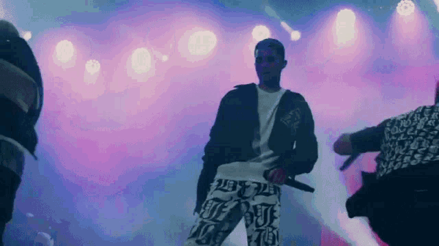 a man is standing on a stage holding a microphone while a group of people are dancing behind him .