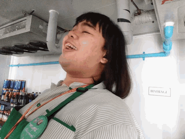 a woman wearing a green apron is laughing in front of a beverage sign
