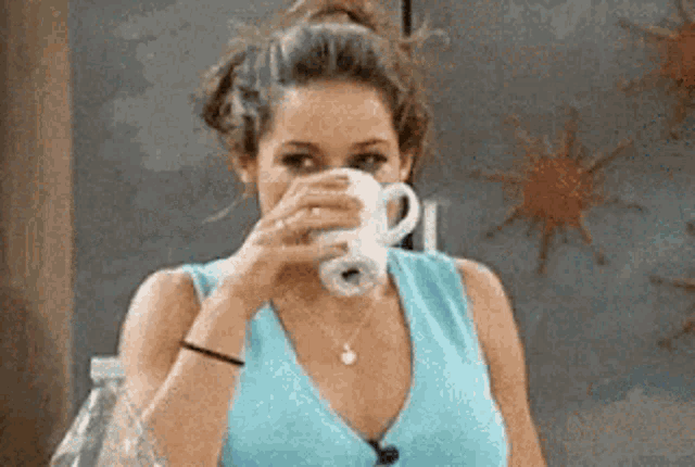 a woman in a blue tank top drinks from a white mug