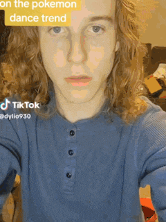 a young man with long curly hair is wearing a blue shirt and a tiktok sticker