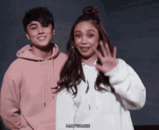 a man in a pink hoodie and a woman in a white hoodie are standing next to each other
