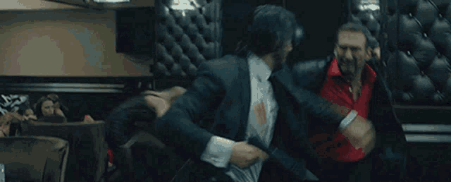 a man in a suit is shooting a gun at another man while another man watches .