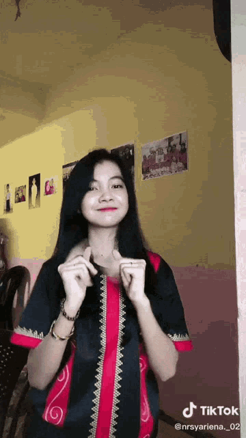 a girl is making a heart shape with her hands while wearing a black and red shirt that says tiktok