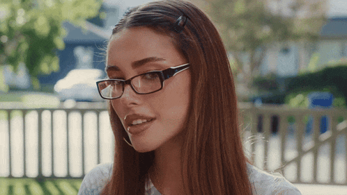 a woman wearing glasses and hoop earrings looks at the camera