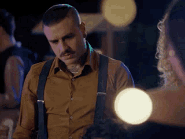 a man with a mustache is wearing suspenders and looking down