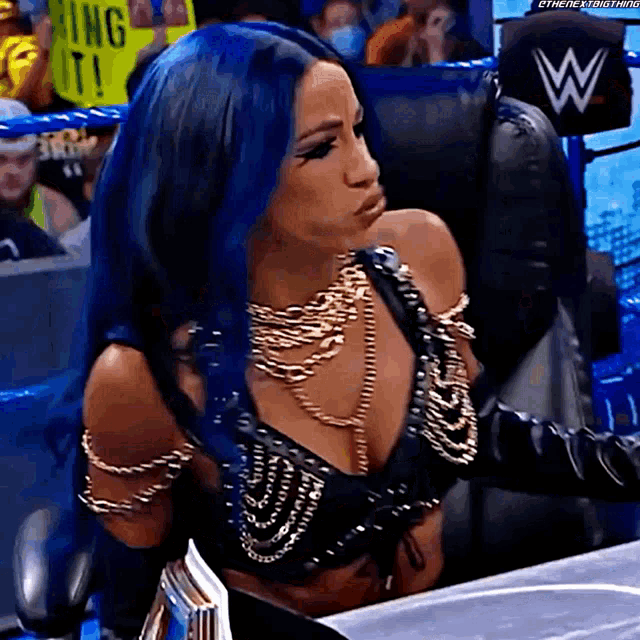 a woman with blue hair is sitting in a chair and making a face .