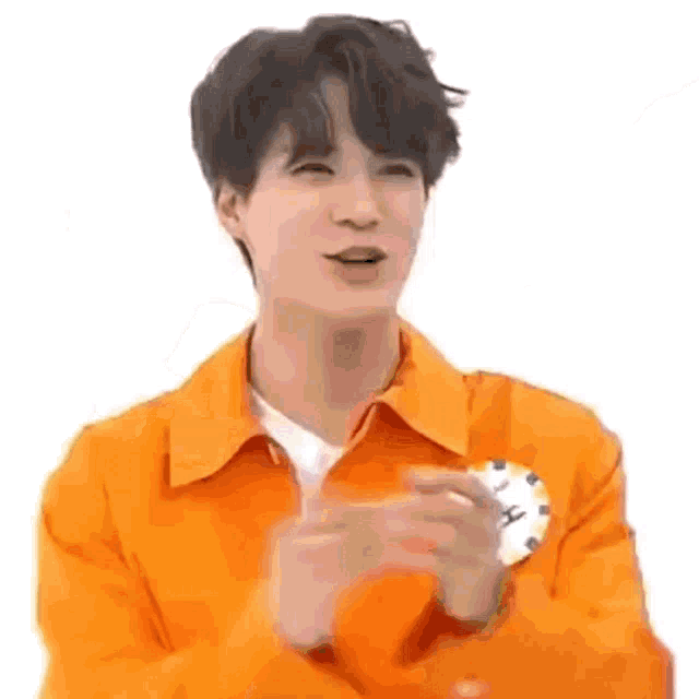 a young man in an orange jacket is clapping his hands in front of a clock .