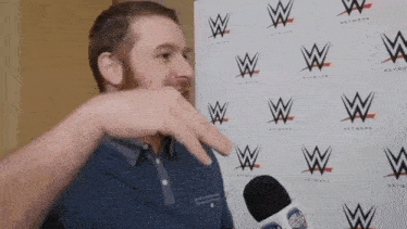 a man with a beard is talking into a microphone in front of a wall with wwe logos on it .