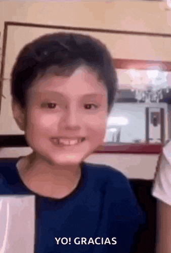 a young boy is smiling and giving a thumbs up sign while wearing a blue shirt .